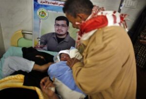 Palestinian baby boy Al-Hassan, the son of Palestinian prisoner Tamer al-Za'an (pictured in poster), who was conceived with al-Za'anin's sperm smuggled out of an Israeli prison, is held by al-Za'an's brother as his mother Hana rests on a bed at a hospital in Gaza City January 10, 2014. REUTERS/Suhaib Salem